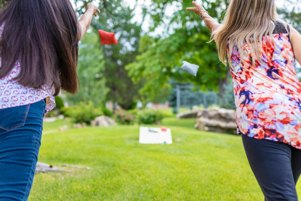 Two girls playing cornhole in their yard.