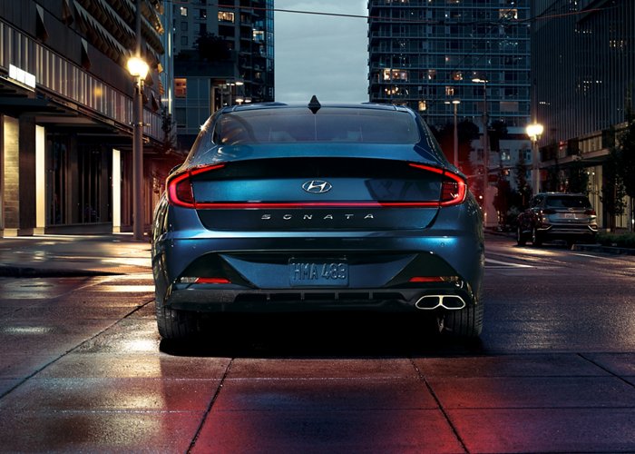 Rear view of a blue 2021 Hyundai Sonata driving down a city street at dusk