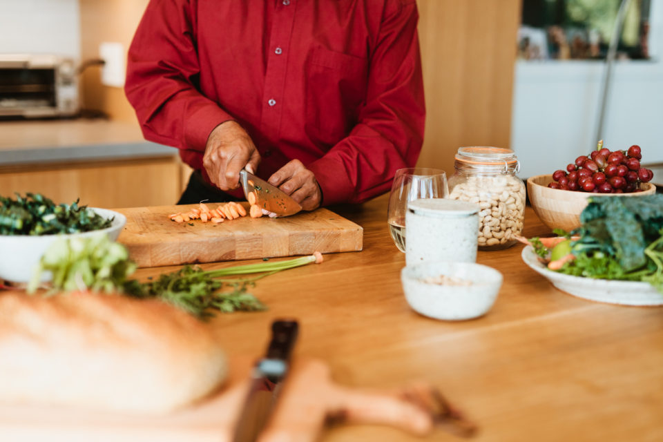 Man chopping carrot on cutting board.