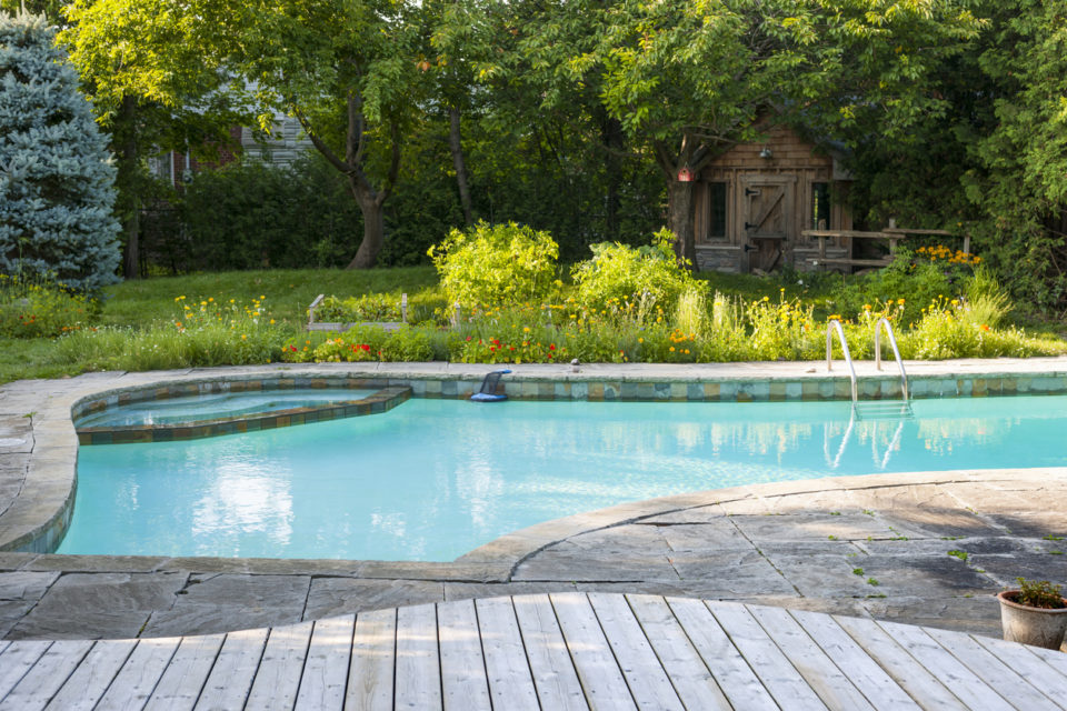 Backyard with outdoor inground residential swimming pool, garden, deck and stone patio