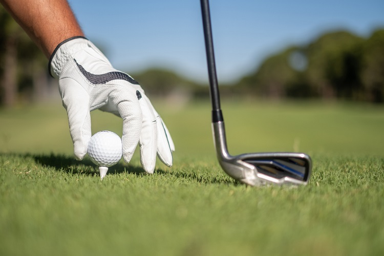 Golfer's hand putting a golf ball on tee in golf course.