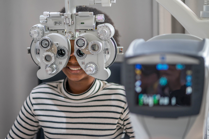 Close-up Of african teen girl Doing Eye Test On Phoropter, African teen girl checking on her eye with optometry machine.