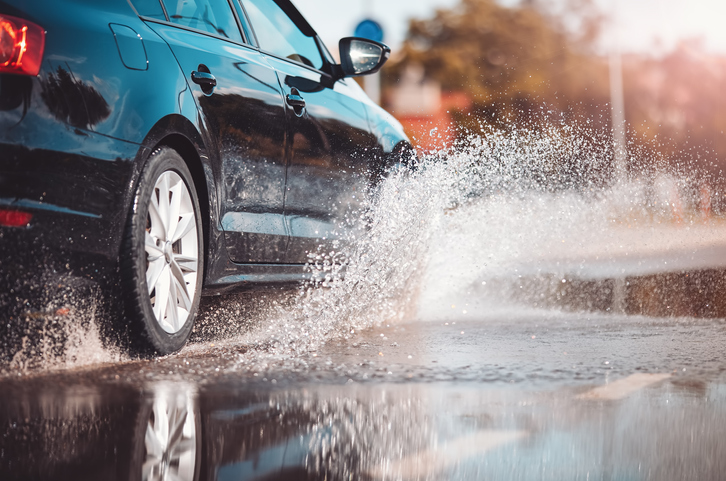 Car driving through the puddle and splashing by water. Dangerous situation. Concept of road safety.