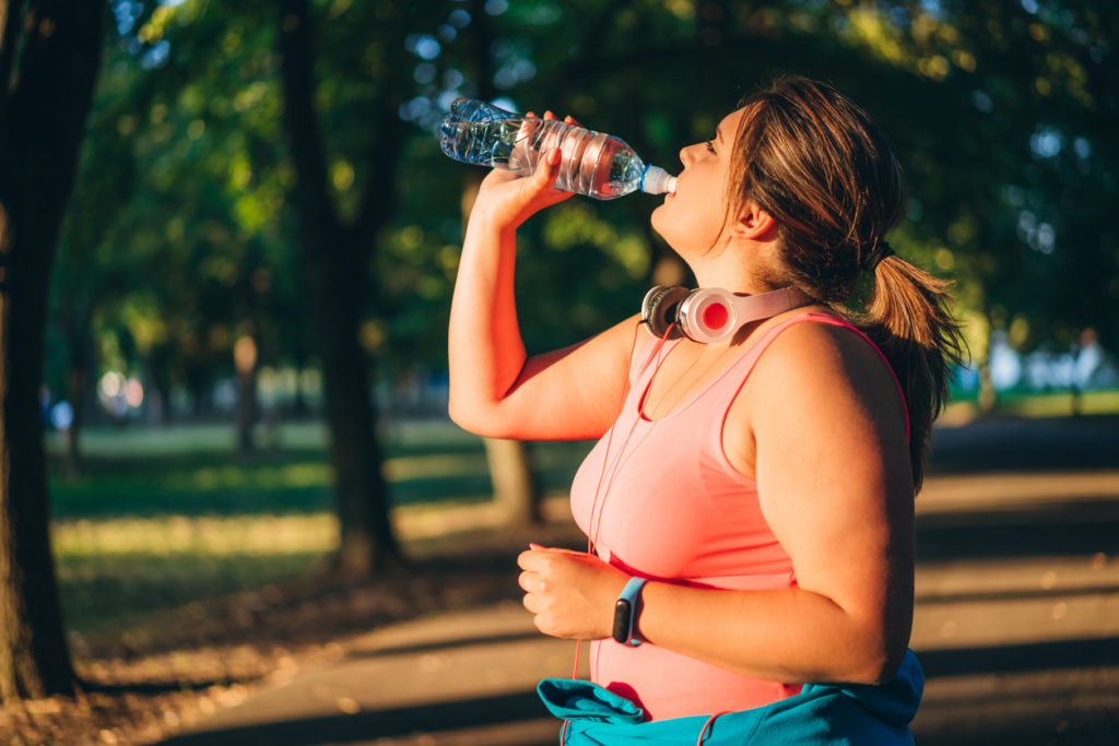 Woman drinking water after running in a public park.