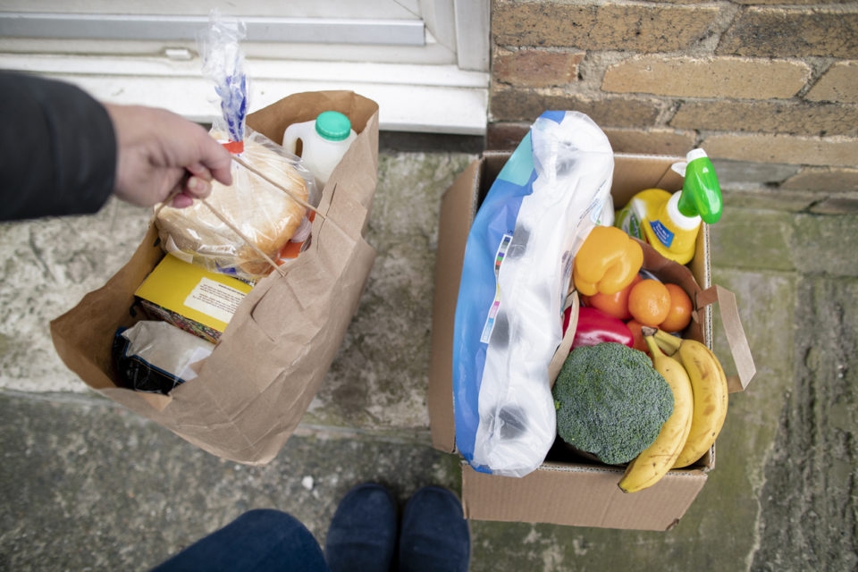 Woman dropping off a box of groceries on doorstep.