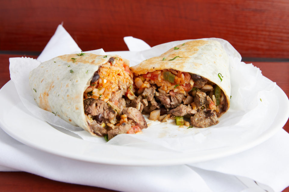 Two halves of a steak burrito on a white plate