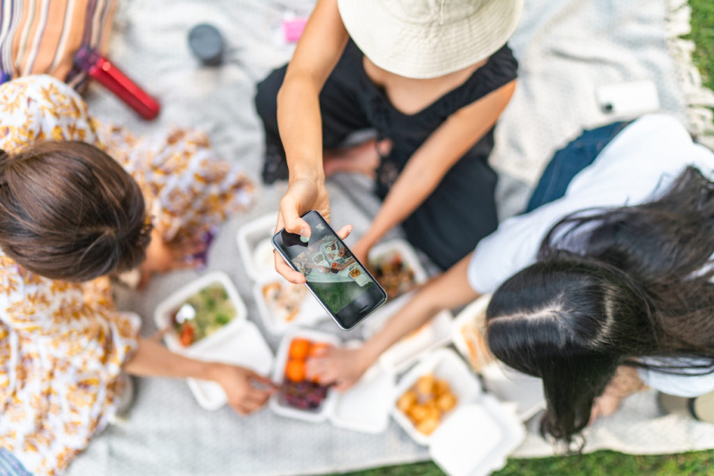 Woman taking photos and videos of food during picnic while preparing food